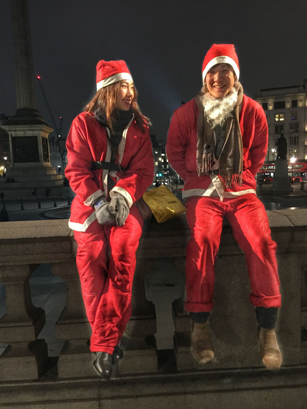 couple in father Christmas outfits sitting on a wall at Trafalgar Square in London
